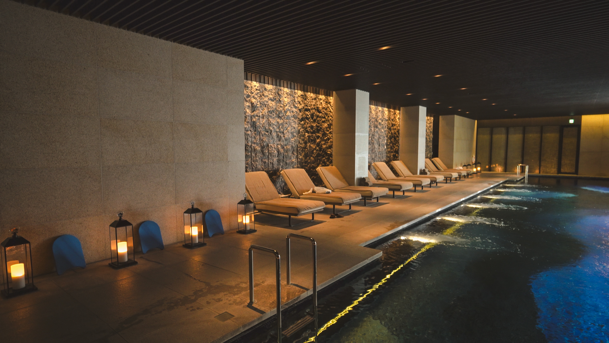 Pool and loungers against a grey wall with serene lighting and a dark roof.