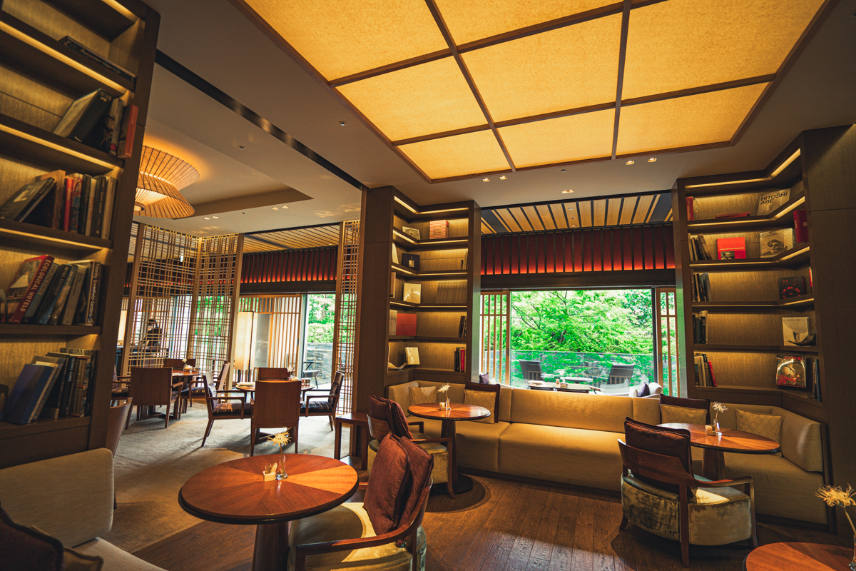 Lobby lounge with sofas, tables and chairs with lush trees outside and seating on balconies.