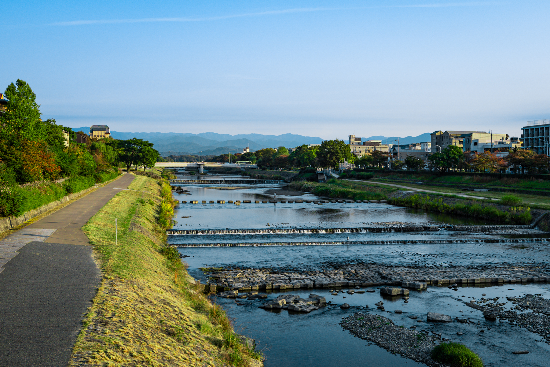 Kamogawa River with stone steps and mountains in the background and blue sky.