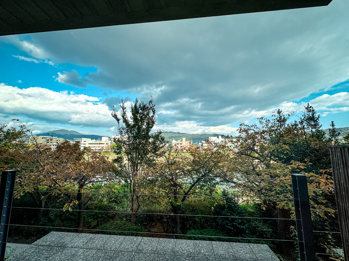 View outside from the balcony with blue sky and clouds and trees covering the Kamogawa River.