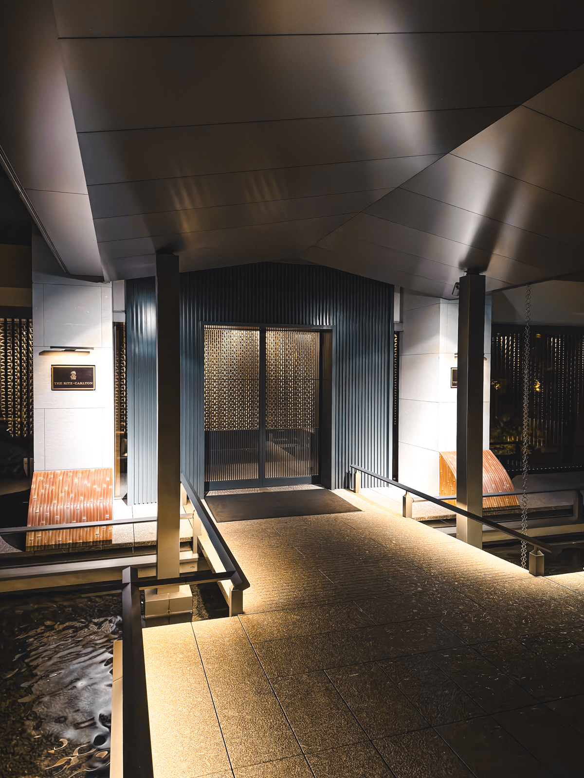 Automatic doors of Ritz-Carlton Kyoto entrance during dusk with lights lighting up the pathway.