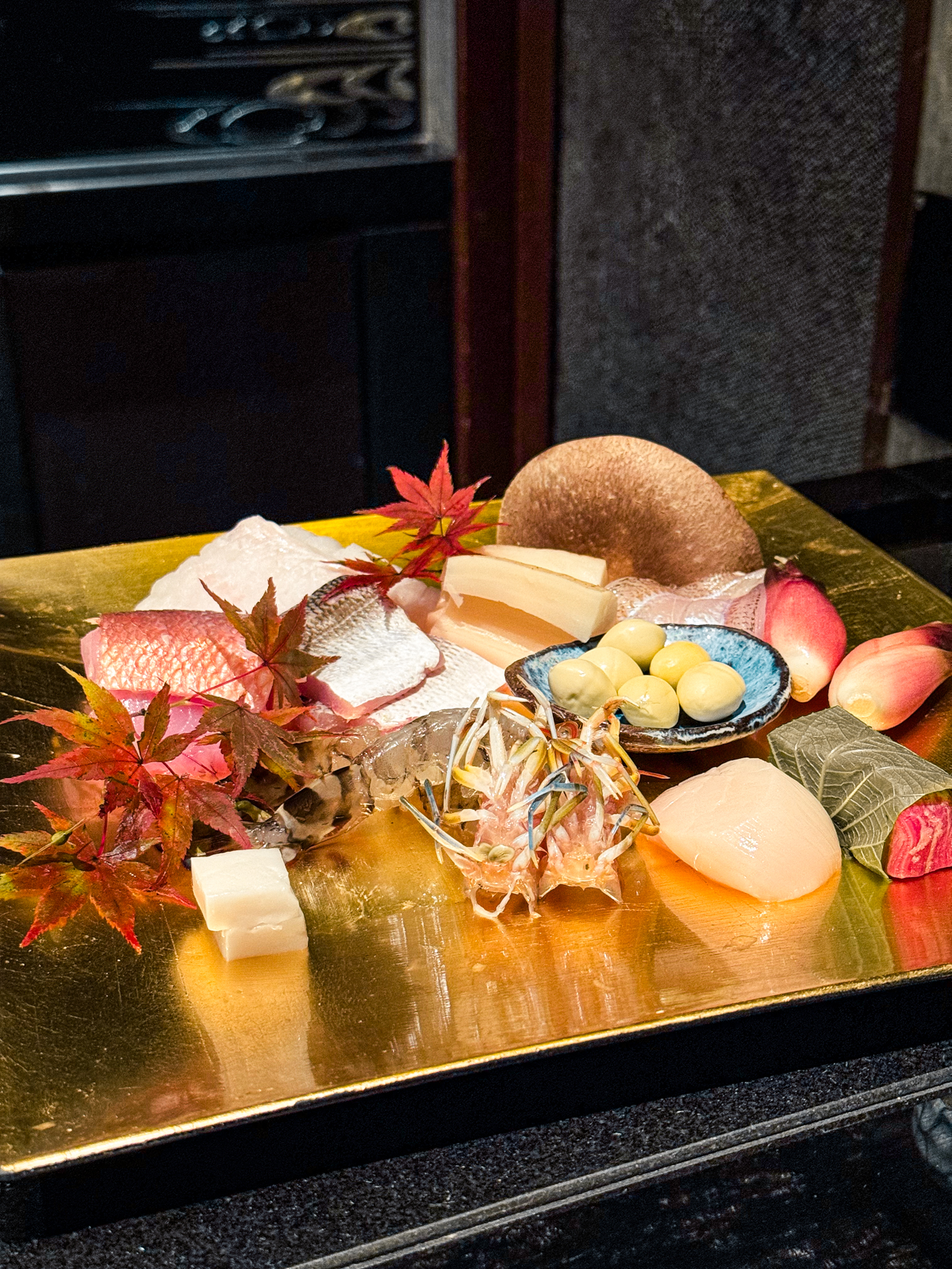 Square plate showcasing all of the raw ingredients for the tempura meal with mushrooms, shimp, wagyu, scallops, fish, lotus root, and more.