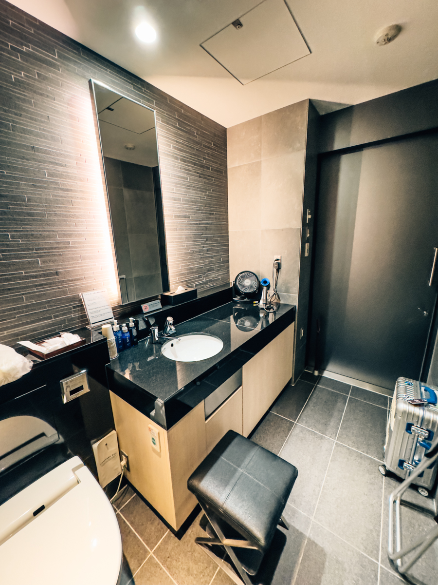 Shower suite with single vanity, sink, Japanese bidet toilet, stool, and Dyson hair dryer.