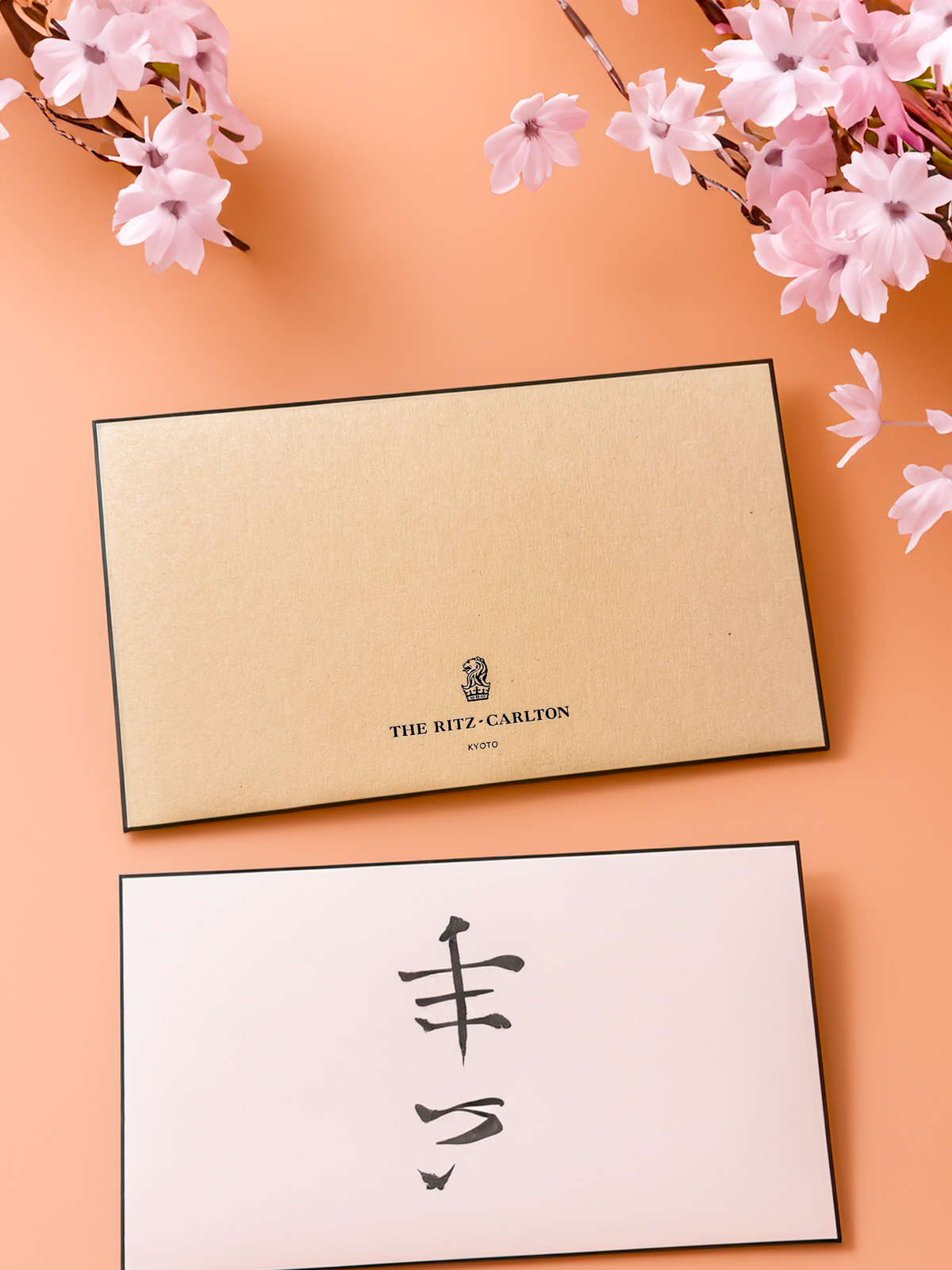 Wooden Ritz Carlton Kyoto branded picture frame with Japanese calligraphy on the bottom flanked with sakura flowers over an orange background.