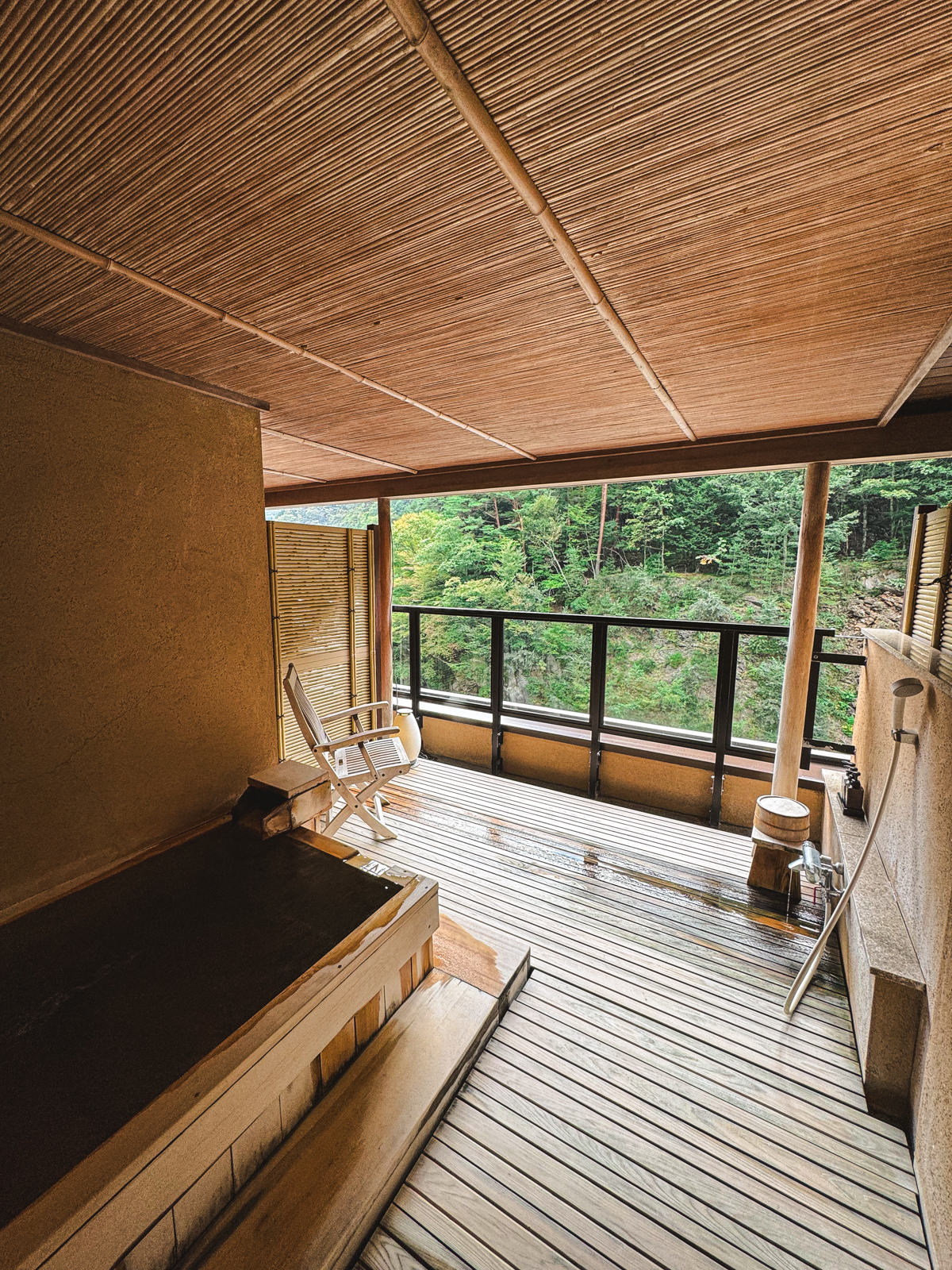 Outdoor onsen surrounded with wooden planks with a forest in background.
