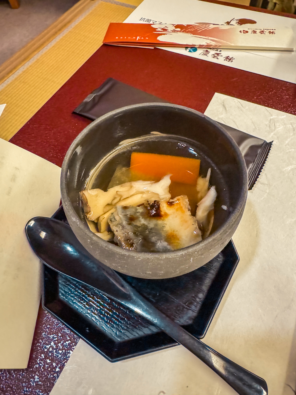 Eel and root vegetable soup in a black stone bowl.