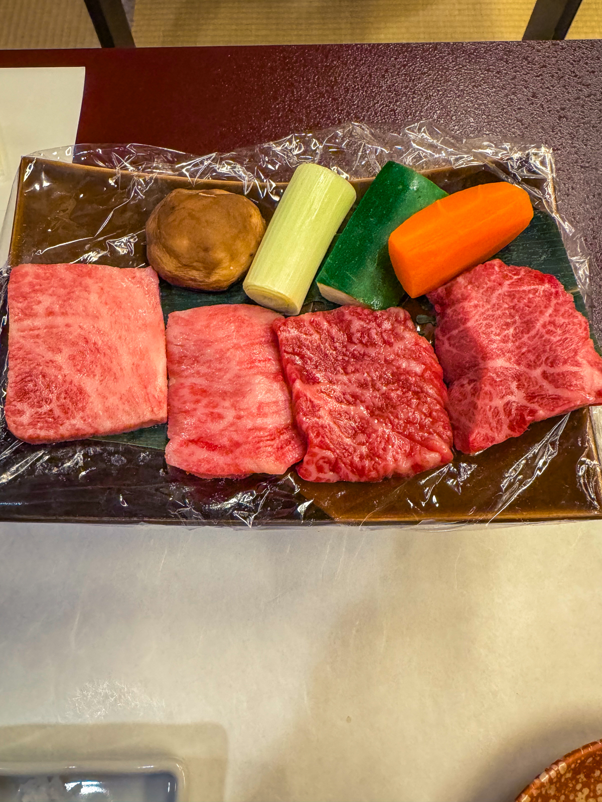 Raw presentation of grill ingredients with 4 pieces of wagyu, mushroom, and veggies.