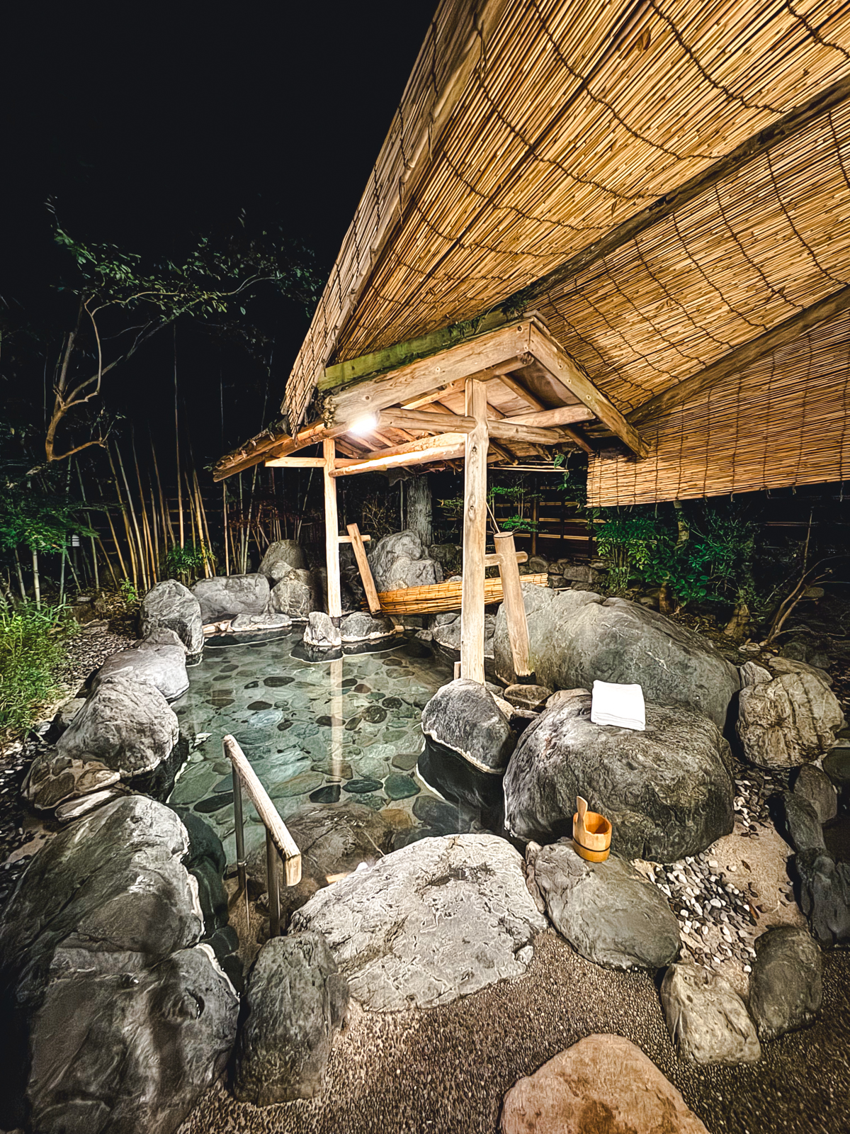 Large stone onsen with wooden roof and a light.